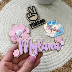 May include: A set of three personalized wooden name tags with pink and purple accents. The names are "Mylana", "Matteo", and "Rylana".