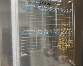 May include: A clear acrylic medication tracker with a grid for recording daily doses. The tracker has a section for AM and PM medications, with columns for the medication name, dose, time, and days of the week. The tracker also includes a section for notes. The text on the tracker reads "MEDICATION TRACKER FOR: Name: Samuel/Hylana Doctor:"