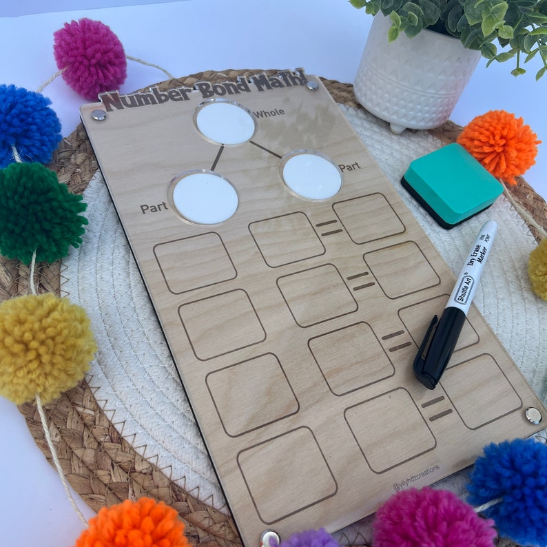 Puede incluir: Un tablero de madera para matem&aacute;ticas de uni&oacute;n de n&uacute;meros con c&iacute;rculos y cuadrados blancos para escribir n&uacute;meros. El tablero tiene las palabras "Number Bond Math" y "Whole", "Part" y "Part" escritas en &eacute;l. Tambi&eacute;n se muestra un marcador de borrado en seco y una goma de borrar.