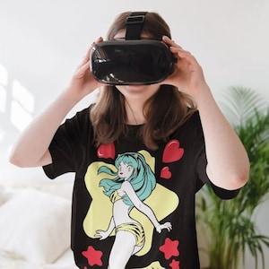 Puede incluir: Una persona lleva una camiseta negra con un gráfico de personaje de anime colorido. El personaje es una mujer con el pelo largo verde y una estrella amarilla detrás de ella. La persona lleva un casco de realidad virtual.