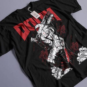 May include: Black t-shirt featuring a graphic of a futuristic warrior with a weapon, in white and red. The word "DOOM" is printed in large red letters. A tag is attached to the shirt.