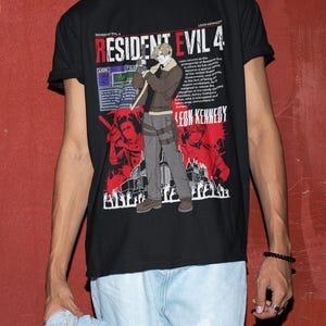 May include: Black t-shirt featuring a graphic print of a video game character holding a gun. The text "Resident Evil 4" is printed in white on the shirt. The character is standing in front of a city skyline. The text "Leon Kennedy" is printed in white at the bottom of the shirt.