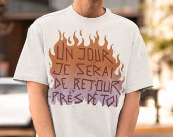 Pode incluir: Camiseta branca com um gráfico de chamas e o texto "Un jour je serai de retour près de toi" em francês.