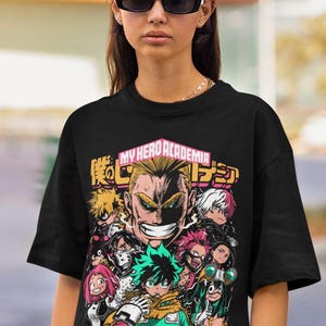 May include: Black t-shirt with a graphic print of characters from the anime My Hero Academia. The graphic features the text "My Hero Academia" in pink and Japanese characters. The characters are depicted in a colorful, stylized design. The text "Plus Ultra" is printed in Japanese characters at the bottom of the graphic.