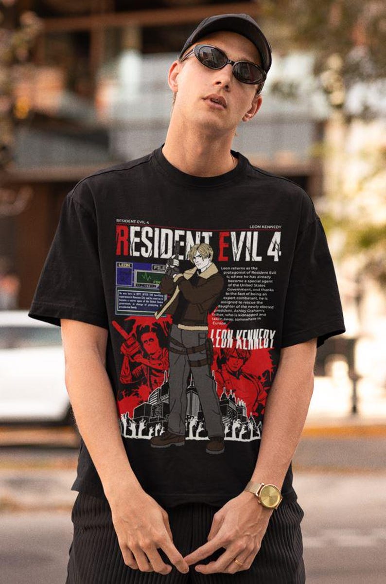 May include: Black t-shirt featuring a graphic print of Leon Kennedy from Resident Evil 4. The graphic includes the game's title, a character portrait, and text describing the game's story.