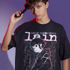 May include: Black t-shirt with a graphic print of a girl with black hair and a black jacket. The text "serial experiments lain" is printed in white on the shirt.