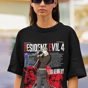 May include: Black t-shirt featuring a graphic print of Leon Kennedy from Resident Evil 4. The graphic includes a video game character holding a knife, a file folder, and text that reads "Resident Evil 4" and "Leon Kennedy".