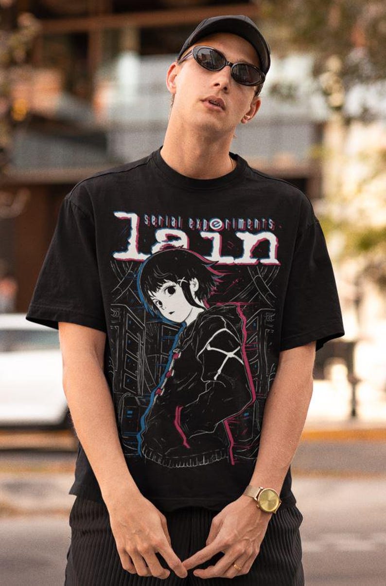 May include: A black t-shirt with a graphic print of an anime character. The graphic is in white, pink, and blue. The text on the shirt reads "serial experiments lain".