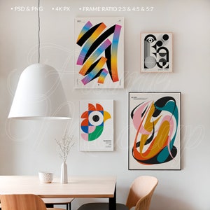 Op de afbeelding: Vier abstracte kunstprints in verschillende kleuren en ontwerpen hangen aan een witte muur. De prints zijn ingelijst in witte en zwarte lijsten. De prints bevinden zich in een woonkamer met een witte lamp die aan het plafond hangt en een houten tafel met twee stoelen.