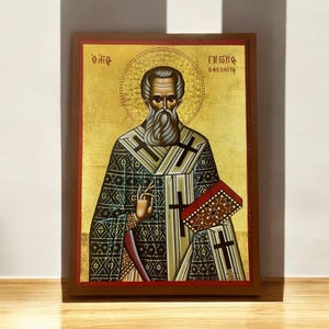 Op de afbeelding: Een ingelijst icoon van Sint Theodorus de Grote, een Grieks-orthodoxe heilige. Het icoon is geschilderd in een traditionele stijl met een gouden achtergrond en een halo rond het hoofd van de heilige. De tekst op het icoon luidt "Ο Άγιος Θεόδωρος" in het Grieks.