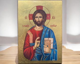 May include: A rectangular religious icon featuring a central figure with brown hair and a beard, wearing a red tunic and blue mantle. The figure holds a book and makes a gesture. The background is gold with a red halo and Greek text.