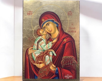May include: A rectangular religious icon painting on a gold background featuring a figure in a deep red hooded robe holding a child in a light-colored patterned garment. Greek text is inscribed on the surface, including the words Glykophilousa.