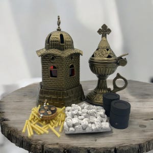 May include: A gold metal incense burner set featuring a church-shaped holder, a censer with a handle, and a small pile of incense charcoal. The set also includes a pack of incense sticks and a small metal incense burner.