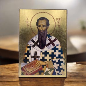 Op de afbeelding: Een religieus icoon met een man met een lange baard, een halo en sierlijke kleding. Het icoon heeft een achtergrond van bladgoud en tekst in een vreemde taal. De man houdt een rood boek vast.