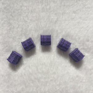 May include: Five small, purple, cube-shaped objects with numbers and letters printed on them. The objects are arranged in a semi-circle. The numbers and letters are white.