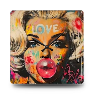 May include: Square wall clock featuring a pop art style portrait of a woman with blonde hair and blue eyes. The word "LOVE" is painted on the forehead. A bubblegum bubble is in front of the lips. The clock hands are black.