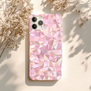 Peut inclure: Une coque de téléphone rose avec un motif géométrique triangulaire. L'étui a une finition brillante et une découpe pour l'appareil photo. Le fond est beige clair avec des ombres de plante.