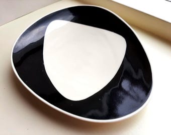Op de afbeelding: Een moderne, abstracte keramische schaal met een unieke vorm. De schaal heeft een witte binnenkant en een opvallende, zwarte rand die een opvallend contrast creëert. Het ontwerp is minimalistisch en stijlvol, geschikt om te serveren of tentoon te stellen. Ongeveer 20 cm in diameter.