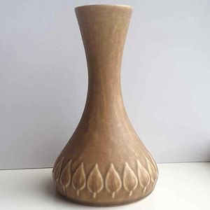 以下が含まれることがあります： 細い首と広い底を持つ茶色の陶器の花瓶。花瓶の底には葉の模様が施されています。