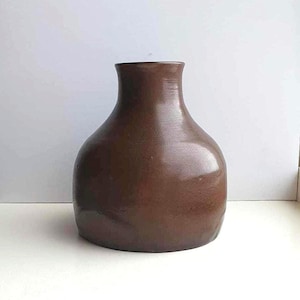 以下が含まれることがあります： 丸みを帯びたボディと狭い首を持つ茶色のセラミック花瓶。花瓶は滑らかで光沢のある仕上げです。