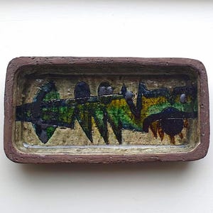 Peut inclure: Un plat rectangulaire en céramique avec un bord brun et un intérieur blanc. Le plat est décoré d'un motif abstrait en vert, bleu et noir.