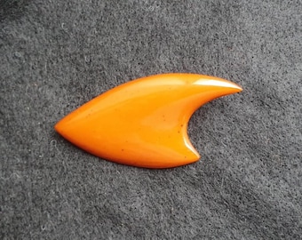 May include: An orange, fin-shaped object with a curved design. The object has a glossy finish and appears to be made of a solid material. The background is a textured gray surface.