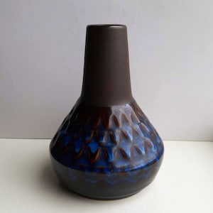 Può includere: Un vaso in ceramica con collo marrone scuro e base bulbosa. La base presenta un motivo strutturato a forma di diamante con sfumature blu e marroni. Il vaso ha una finitura lucida.