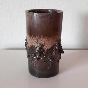 May include: A cylindrical brown ceramic vase with a textured, rough surface near the base. The vase has a smooth, glossy finish on the upper portion and a lighter, speckled band between the smooth and textured areas.