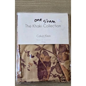 May include: A Calvin Klein King size pillow sham from The Khaki Collection. The pillow sham is beige with a floral pattern in shades of brown and burgundy. The packaging reads "one sham".