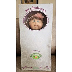 May include: A Cabbage Patch Kids 20th Anniversary doll in its original box. The doll has a round face, green eyes, and a pink flower in its hair. The box features the text "20th Anniversary" and "2003 Edition Cabbage Patch Kids."