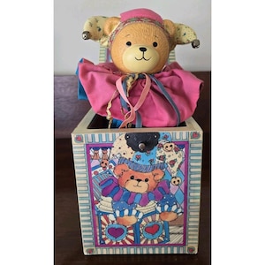 May include: A white ceramic mug with a black handle and the text "But First, Coffee" in a bold, black font. The mug is set against a blurred background, suggesting a cozy setting.