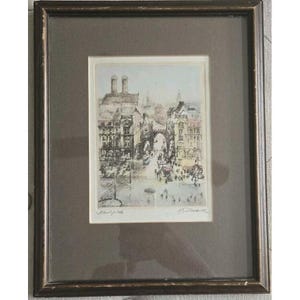 May include: Framed print of a European city scene. The artwork depicts a street with buildings, an archway, and people. The print is in muted tones of beige, gray, and brown, with a dark brown frame and a gray mat.