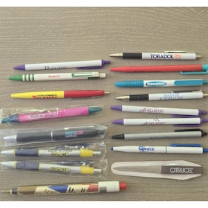 May include: A collection of various promotional ballpoint pens featuring pharmaceutical brand names like Toradol, Nasonex, Tylenol, and Relafen, alongside a Citrucel nail file, with some pens encased in clear plastic protective sleeves.