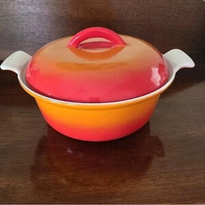 May include: A round, enameled cast iron Dutch oven with a lid. The pot is a gradient of yellow to red-orange, with a red handle on the lid. It has white handles on either side.