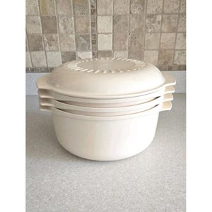 May include: A stack of four off-white, round food storage containers with lids. The containers have handles and a ridged lid for ventilation. The set is made of durable plastic and is designed for kitchen use.