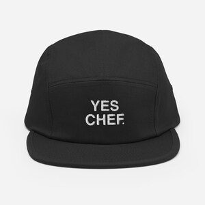 May include: Black 5-panel camp cap with white embroidered text that reads "YES CHEF."