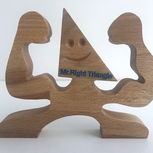 May include: Wooden sculpture of a person with two arms raised, holding a triangle with a smiling face and the text "Mr. Right Triangle" on it.