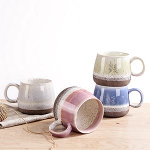 Peut inclure: Plusieurs tasses en céramique de différentes couleurs, dont blanc, rose, bleu et vert. Chaque tasse a une finition tachetée et texturée et une base marron. Certaines tasses ont du texte et des motifs floraux.