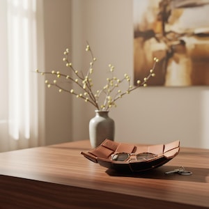 May include: A square, tan-colored, woven-style tray holds a pair of tortoise-shell sunglasses and a set of metal keys. The tray features a grid-like pattern with folded edges, providing a shallow container for small personal items.