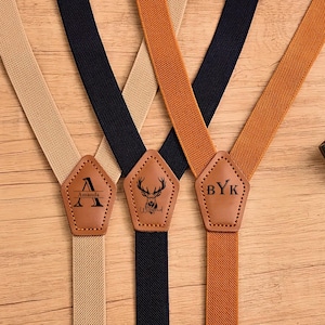 Puede incluir: Tres pares de tirantes en beige, azul marino y naranja. Cada tirante tiene un parche de cuero marrón con un diseño personalizado. Un parche tiene la letra "A" y el nombre "Amanda", otro una ilustración de ciervo y el último las iniciales "BYK".