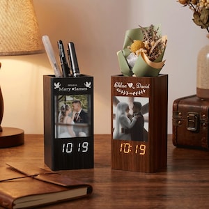 Peut inclure: Deux organisateurs de bureau rectangulaires en bois avec horloges numériques intégrées. L'organisateur de gauche est en bois foncé avec une photo de couple, la date 2023-02-14 et deux stylos. Celui de droite est en bois clair avec des fleurs séchées.