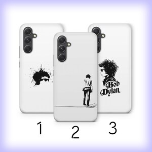 May include: Three white phone cases with different designs. The first case has a black splatter paint design. The second case has a black silhouette of a person. The third case has a black and white illustration of Bob Dylan with the text "Bob Dylan".