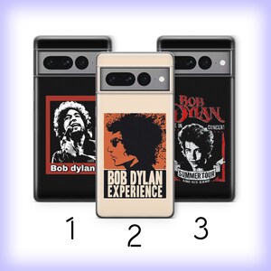 May include: Three different phone cases featuring images of Bob Dylan. The first case has a black background with a red and white image of Bob Dylan singing into a microphone. The second case has a cream background with a black and white image of Bob Dylan with a guitar. The third case has a black background with a black and white image of Bob Dylan with the text "Bob Dylan" and "Summer Tour and His Band".
