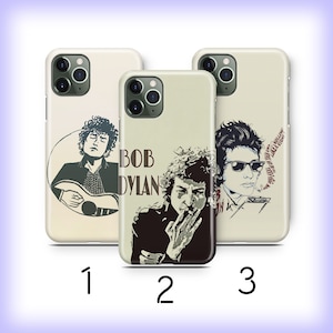 May include: Three different phone cases featuring images of Bob Dylan. The first case shows Dylan playing a guitar, the second case shows Dylan smoking a cigarette, and the third case shows Dylan wearing sunglasses.