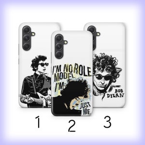 May include: Three white phone cases with different designs featuring black and white illustrations of Bob Dylan. The first case has a black and white illustration of Bob Dylan playing a guitar. The second case has a black and white illustration of Bob Dylan with the text "I'm no role model I'm just me". The third case has a black and white illustration of Bob Dylan with the text "Bob Dylan".