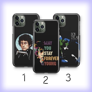 May include: Three black iPhone cases with different designs featuring Bob Dylan. The first case has a colorful portrait of Bob Dylan playing a harmonica. The second case has a colorful portrait of Bob Dylan with the text "May You Stay Forever Young". The third case has a black and white portrait of Bob Dylan with the text "Bob Dylan & His Band".