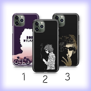 May include: Three phone cases featuring Bob Dylan designs. The first case is purple with a silhouette and motorcycle graphic. The second case is black with a white graphic and text. The third case is black with a sepia-toned image of Bob Dylan.