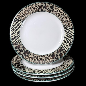 Op de afbeelding: Set van vier witte keramische borden met een decoratieve dierenprintrand. De rand heeft een combinatie van zebra strepen en luipaardvlekken in bruin, beige en zwart. Elk bord heeft een dunne groene rand.