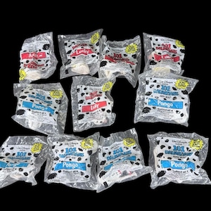 Könnte beinhalten: Eine Sammlung versiegelter McDonald's Happy Meal-Spielzeuge mit Charakteren aus Disneys 101 Dalmatiner. Jede transparente Plastiktüte enthält eine kleine, weiße Dalmatinerfigur mit schwarzen Flecken. Einige Tüten sind mit "Lucky" oder "Pongo" beschriftet.