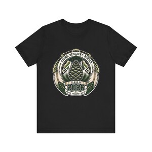 May include: A black short-sleeve t-shirt featuring a circular graphic with a pinecone, a graduation cap, and two feathers. The text reads RISING. RESILIENT. ROOTED. CLASS OF 2026 PROUD. EDUCATED. NATIVE. The design uses shades of green, cream, and black.
